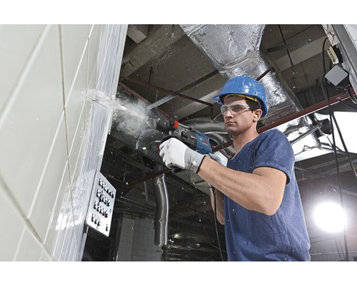 Ein Bauarbeiter bohrt mit einem Bohrhammer in eine Wand.