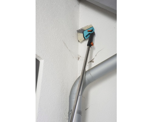 Brosse de façade avec manche télescopique en utilisation sur un mur de maison