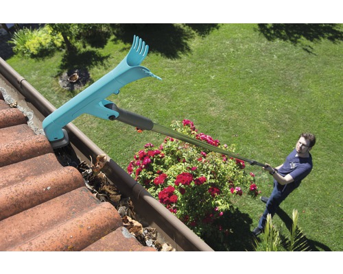 Un homme nettoie une gouttière avec un nettoyeur de gouttière, en enlevant les feuilles.