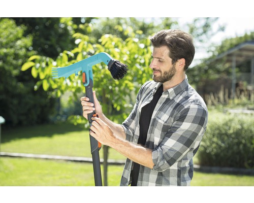 Un homme examine une brosse de jardin télescopique avec raccord d''eau dans le jardin.