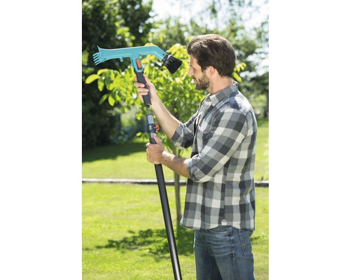 Homme avec une brosse de jardin à manche télescopique dans le jardin.