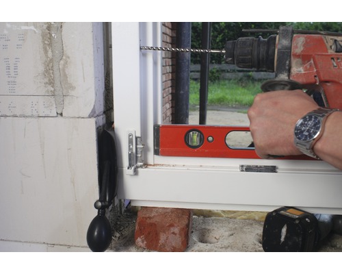 Ein Fenster wird mit einer Bohrmaschine und einer Wasserwaage eingebaut.