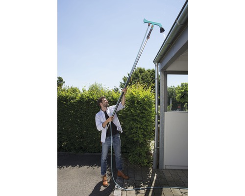 Un homme nettoie une gouttière avec un nettoyeur de gouttière et un manche télescopique.