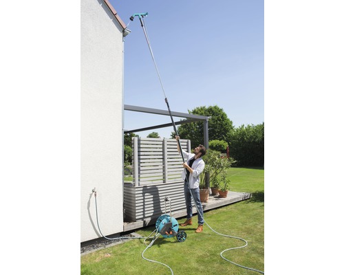 Un homme nettoie une gouttière avec un nettoyeur de gouttière sur un manche télescopique