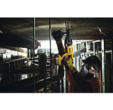 Un ouvrier perce un plafond avec un perforateur. Les tuyaux et la structure métallique sont visibles.