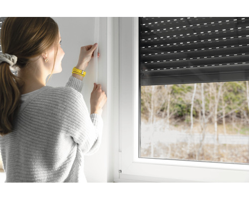 Frau montiert Rollladenführungsschiene am Fensterrahmen