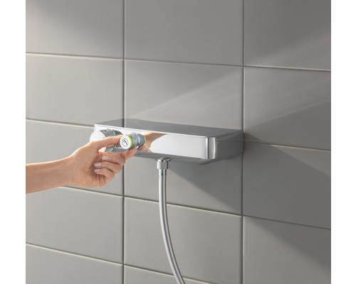 Mitigeur thermostatique apparent avec flexible de douche sur un mur carrelé, la température est réglée.