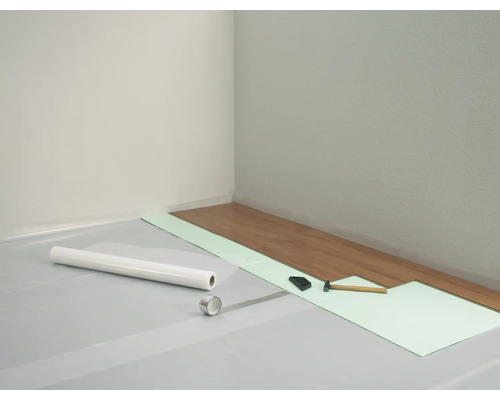 Scène de pose de stratifié, comprenant isolation phonique, pare-vapeur, marteau et tire-lame.