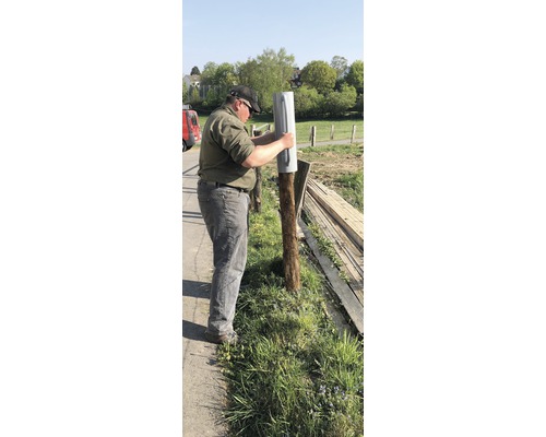 Un homme fixe un support de poteau sur un poteau en bois dans le jardin