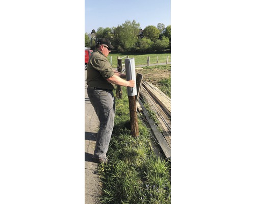 Une personne fixe un sabot de poteau à un poteau de clôture.