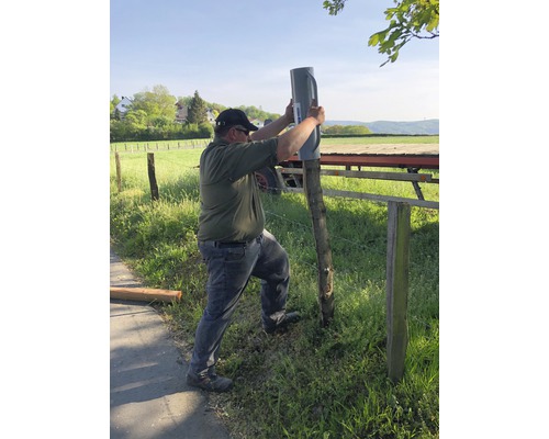 Une personne fixe un support de poteau à un poteau de clôture à l''extérieur.