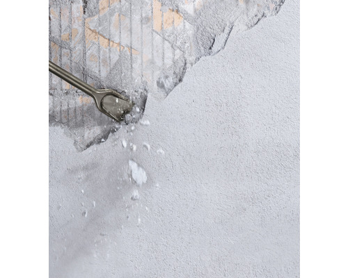 Meißel bearbeitet eine graue Wand und es entstehen Steinsplitter.