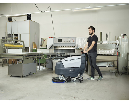 Un homme utilise une autolaveuse Nilfisk SC351 dans un atelier.