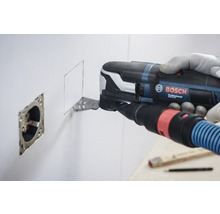 Un homme utilise un outil multifonction Bosch pour découper une ouverture carrée dans un mur à côté d''une prise de courant.