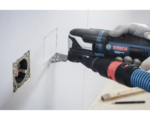 Un homme utilise un outil multifonction Bosch pour découper une ouverture carrée dans un mur à côté d''une prise de courant.