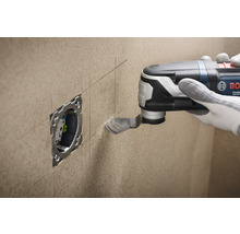 Une personne découpe une ouverture pour une prise de courant dans un mur avec un outil multifonction.