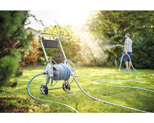 Gartenszene mit Schlauchwagen und Person beim Bewässern des Rasens