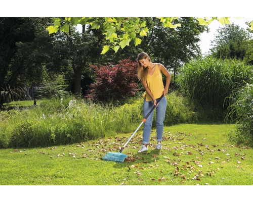Femme ratissant les feuilles mortes avec un balai à feuilles dans le jardin.