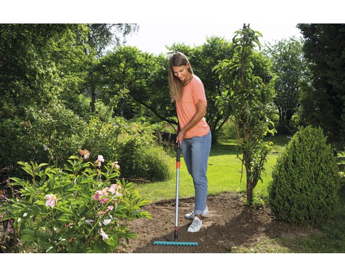 Une femme ratisse le sol dans le jardin avec un râteau