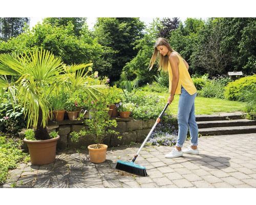 Femme balayant une terrasse en pierre avec un balai de rue dans un jardin
