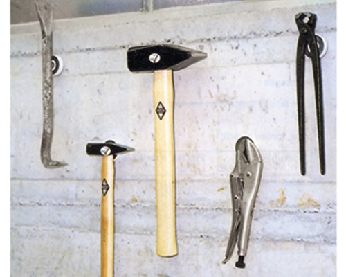 Verschiedene Werkzeuge, darunter Hammer, Brecheisen, Zange und Schraubzwinge, sind an einer Wand aufgehängt