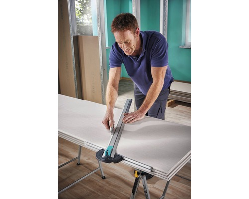 Un homme coupe une plaque de plâtre avec un coupe-plaque de plâtre sur une table.