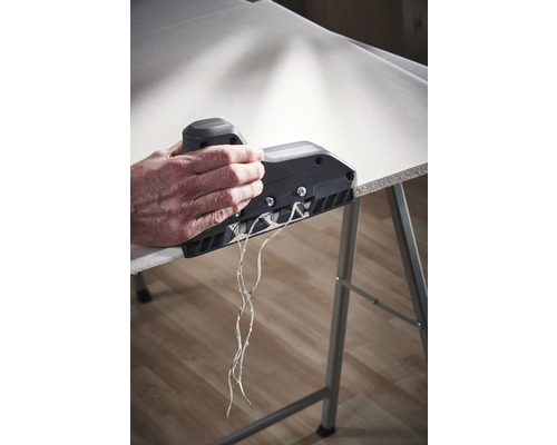 Une personne utilise un rabot à bord sur une plaque de plâtre pour créer un bord propre.