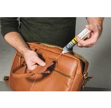 Une personne répare un sac en cuir marron avec de la colle UHU Turbo Fix 2.