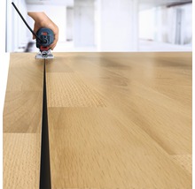 Une main guide une défonceuse le long d''un plan de travail en bois pour fraiser une rainure.