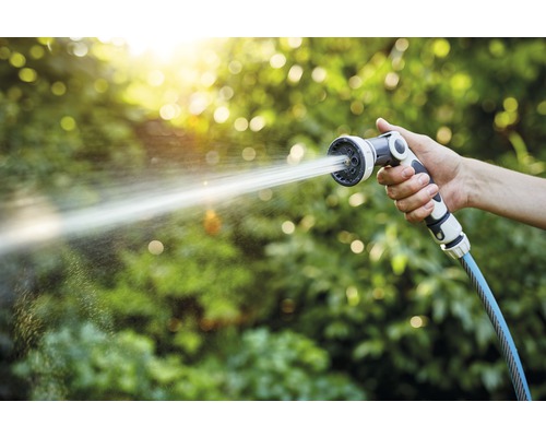 Eine Hand hält einen Gartenschlauch mit Sprühkopf, aus dem Wasser spritzt
