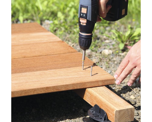 Une personne visse une terrasse en bois avec un tournevis sans fil.