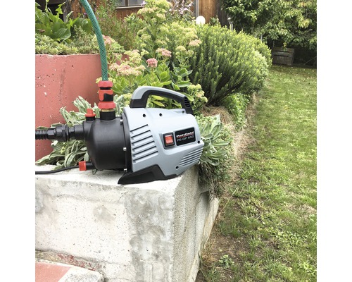 Gartenpumpe mit Schlauch auf einem Betonsockel im Garten