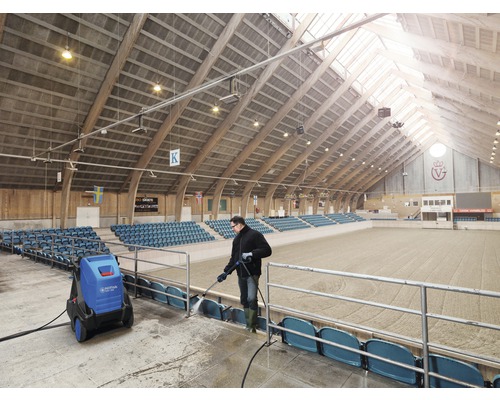 Un homme nettoie les gradins d''un manège avec un nettoyeur haute pression