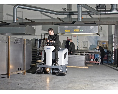 Balayeuse autoportée dans un hall d''usine avec un homme qui la conduit