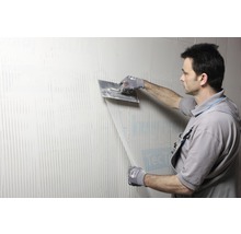 Un homme lisse un mur avec du mastic et une spatule.