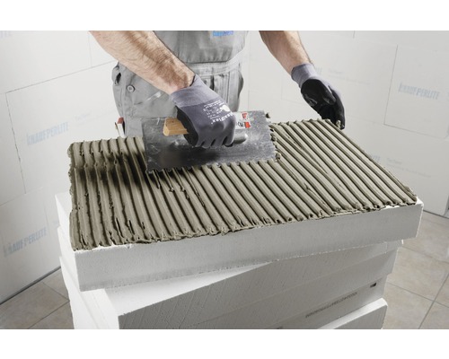 Ein Arbeiter trägt mit einer Glättkelle Klebstoff auf eine Dämmplatte auf.