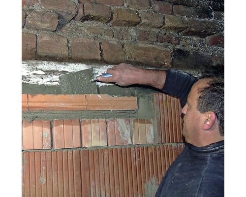 Mann verputzt eine Ziegelwand mit Mörtel und einer Maurerkelle.