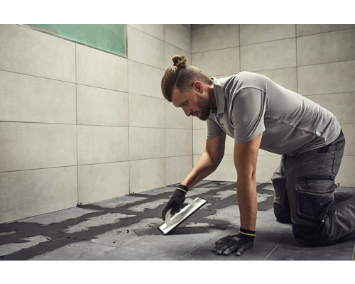 Un homme pose des carreaux avec une spatule dans la salle de bain.