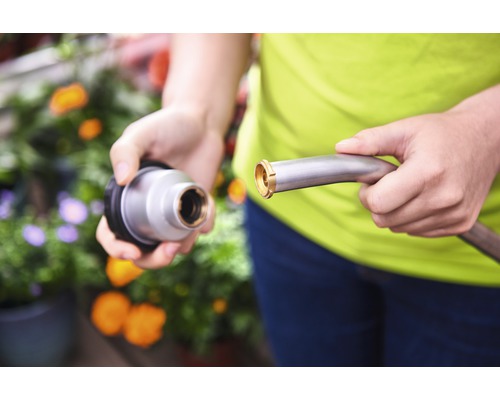 Une personne connecte un tuyau d''arrosage métallique à un embout d''arrosage.