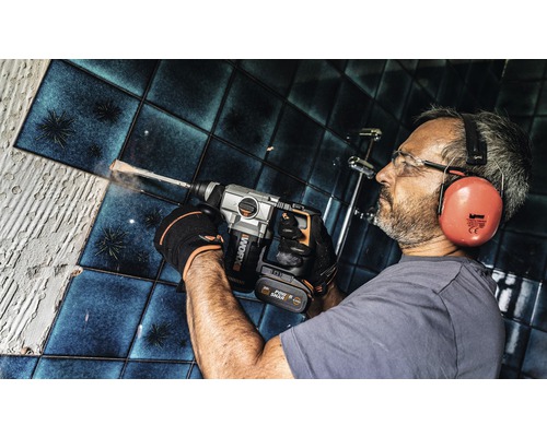 Mann bohrt mit einem Bohrhammer in einer Badezimmerwand mit Fliesen