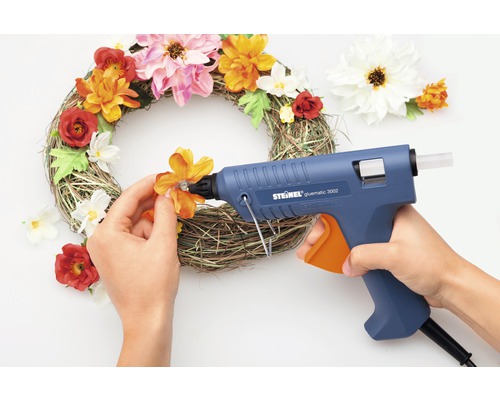 Dekorativer Kranz wird mit Heißklebepistole und künstlichen Blumen verziert.