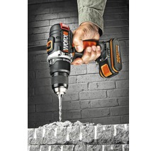 Une main tient une perceuse-visseuse sans fil Worx qui perce une brique.