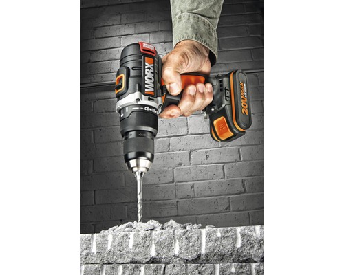 Une main tient une perceuse-visseuse sans fil Worx qui perce une brique.