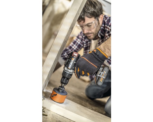 Un homme perce un trou dans un cadre en bois avec une perceuse-visseuse sans fil