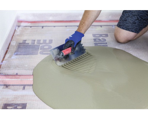 Fliesenleger trägt Fliesenkleber auf Entkopplungsmatte auf