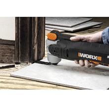 Eine Person verwendet ein Multifunktionswerkzeug von WORX, um eine Fliese neben einem Holzrahmen zu schneiden.