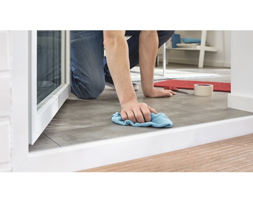 Une personne agenouillée nettoie un sol carrelé avec un chiffon.