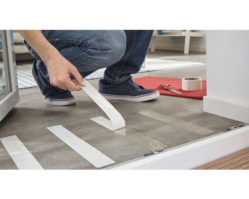 Une personne pose du ruban adhésif sur le sol afin de préparer des travaux de rénovation.