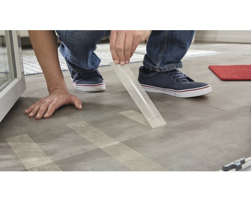 Une personne fixe du ruban en tissu de fibre de verre sur un sol.