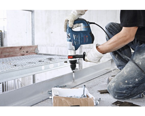 Ein Mann bohrt mit einer Bohrmaschine in ein Metallstück. Schrauben und Dübel liegen bereit.